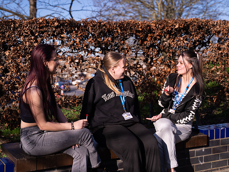 Three students sat on a wall chatting together