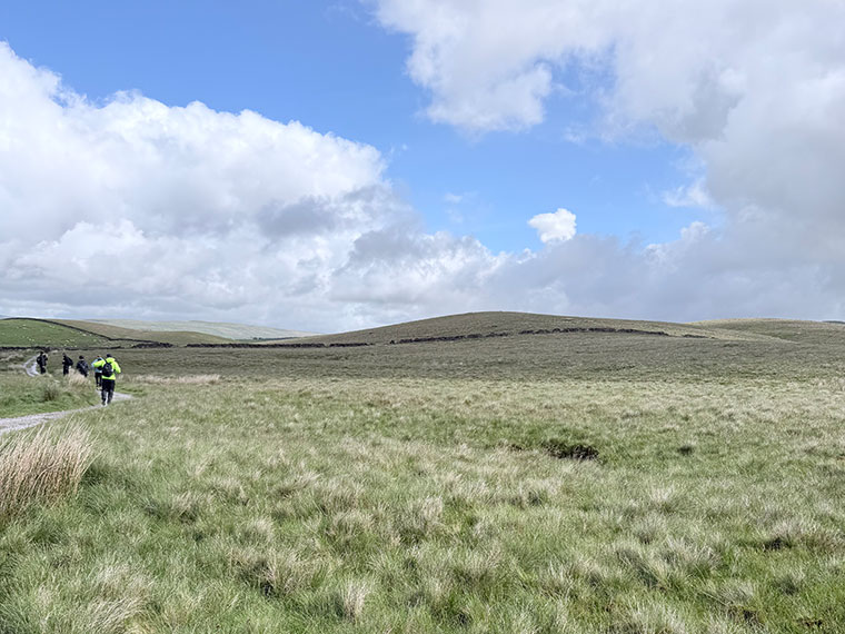 Grass and hills with blue sky with white clouds, people walking away in the distance