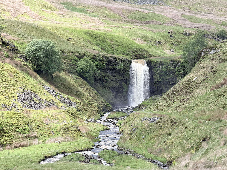 Hills with green grass, a waterfall in the background flowing down between the hills