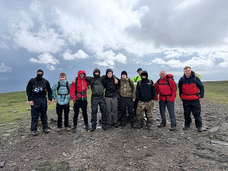 A group of people wearing walking gear stood in a line on a stoney path, clouds in the blue sky behind them