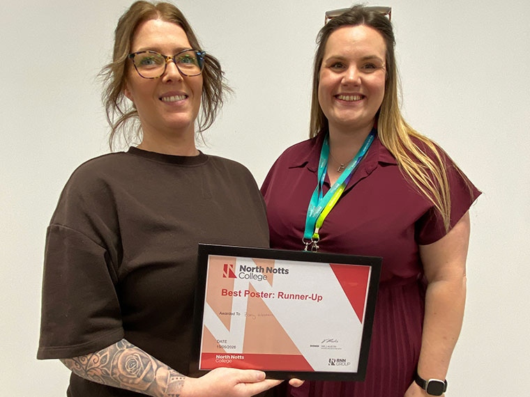 Two females, one wearing a brown top the other wearing a maroon dress, stood together holding a certificate between them