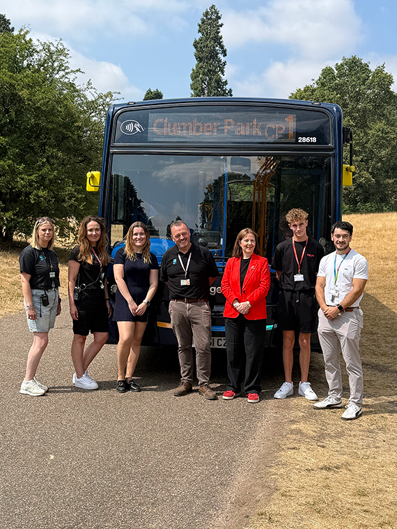 Seven people stood in a line in front of a bus, the bus's desination reading 'Clumber Park'
