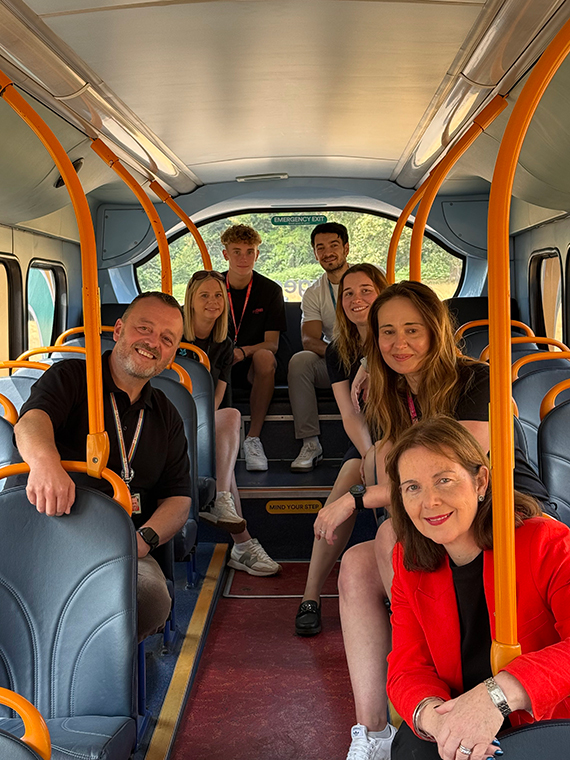 Seven people seated on a bus and smiling at the camera