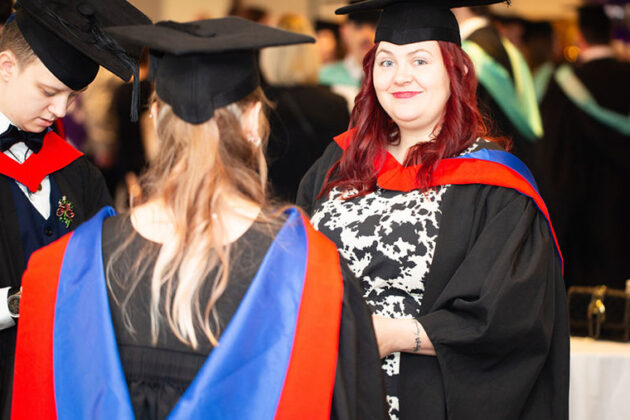 Three people stood together each wearing graduation attire with red, blue ad black colours