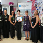 Seven females stood in a line in front of a Rotherham College pull up banner, the person in the centre is holding a certificate