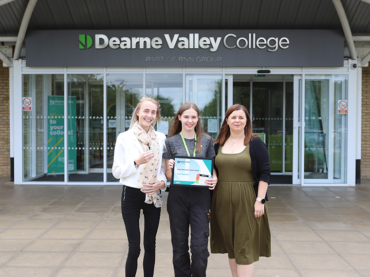 Three females stood together outside the Dearne Valley College building, the person in the centre holding a certificate