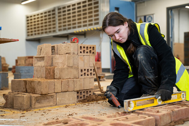 A female in a high vis jacket knelt down checking brick with a spirit level