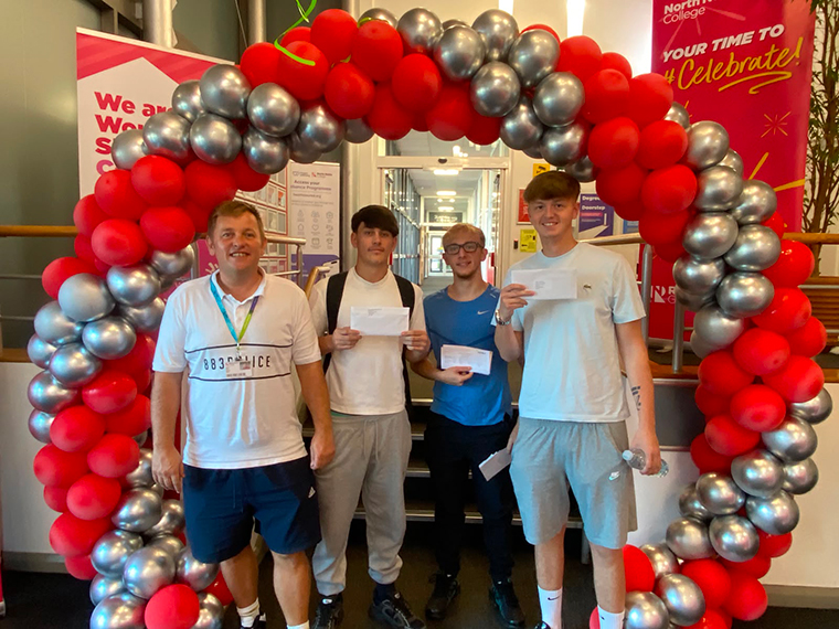 For males stood at the foot of some stairs under a red and silver balloon arch