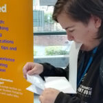 Someone holding a piece of paper in their mouth whilst looking down at other sheet of paper in their hands