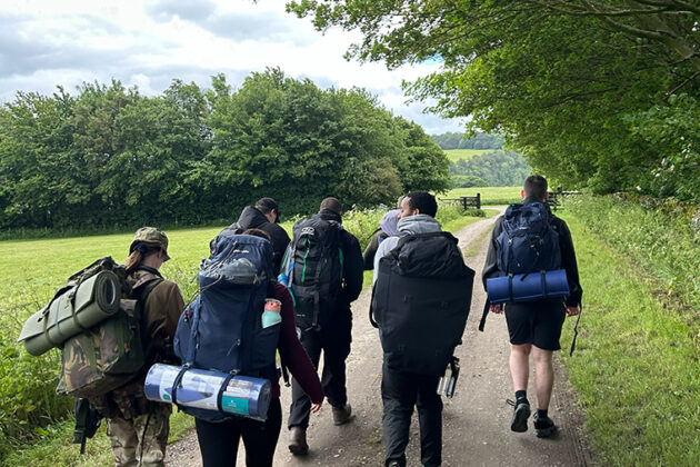 A group of people holding backpacks walking down a path with trees either side