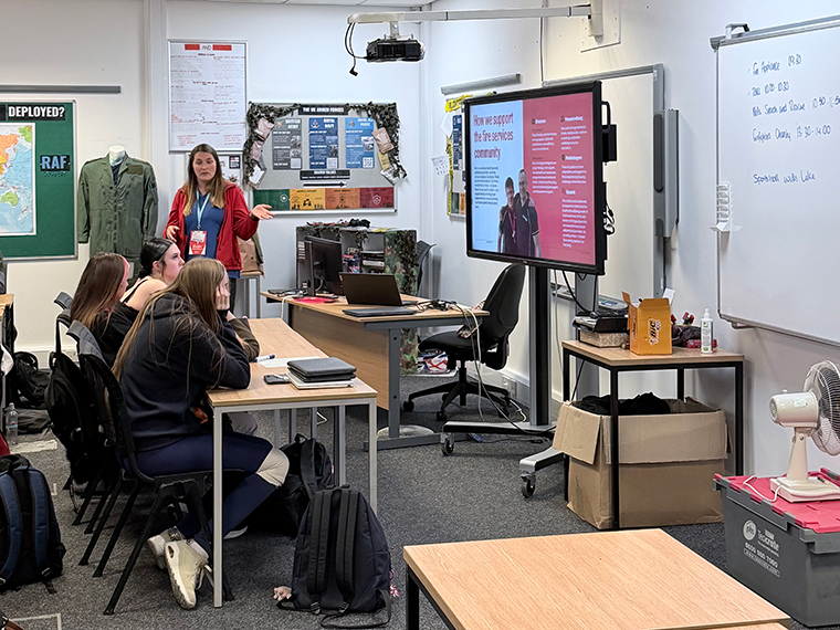 A female stood at the front of a classroom presenting to students sat at tables