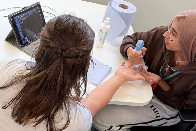 Two females sat at a white table using medical equipment