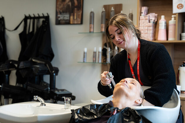 A female dressed in black washing a client's hair over a white sink