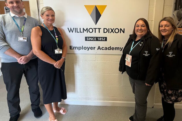 A sign that reads 'Welcome to Willmott Dixon Since 1852 Employer Academy' two people stood at each side of the sign