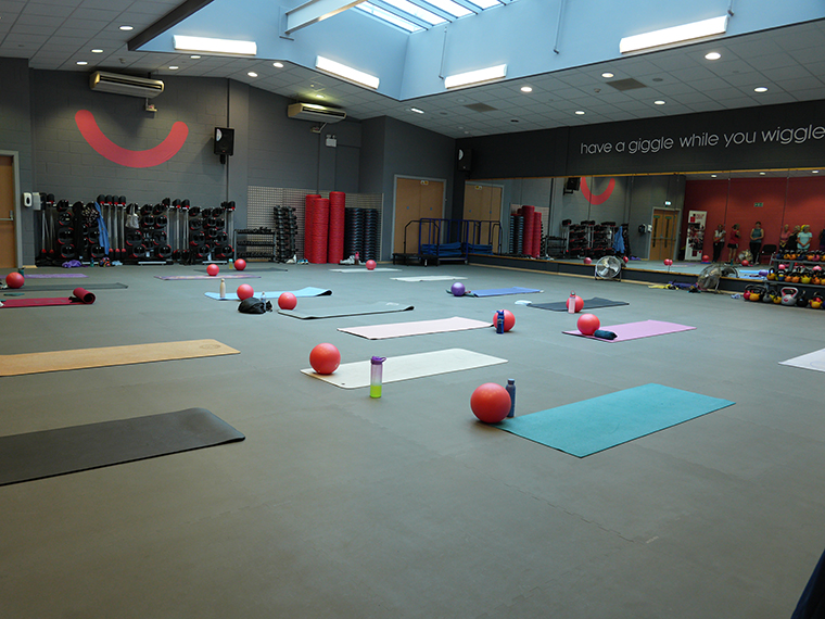 A large gym space with lots of yoga mats on the floor and small balls and drinks bottles