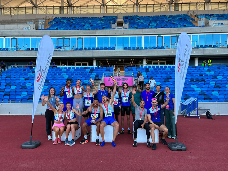 A group of people wearing athletic clothing, each wearing a medal around their necks, the blue seating of a stadium in the background