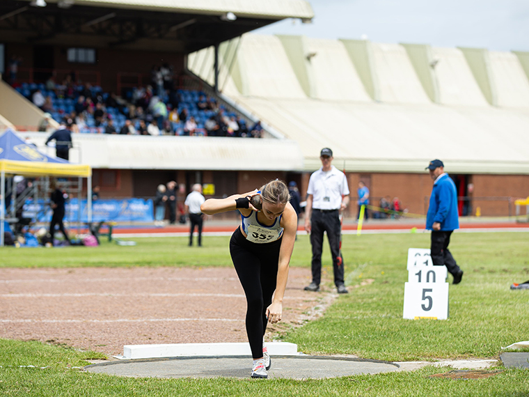 A female about to throw a shot put within a stadium grounds
