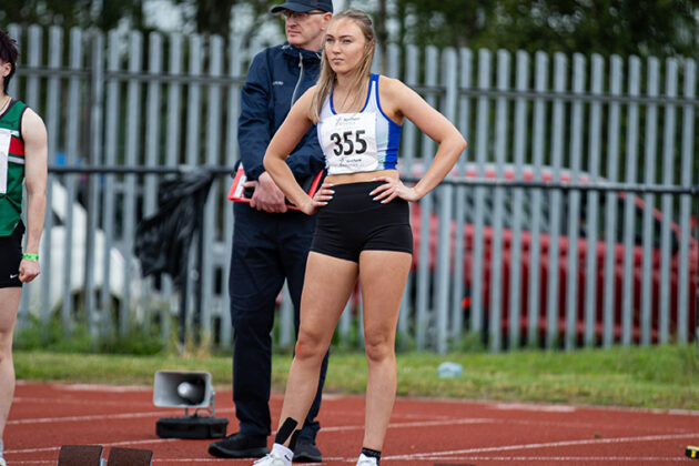 A female with blonde hair and hands on hips stood on a running track