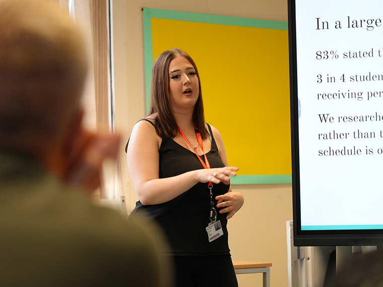 A female stood next to a large white screen presenting to the room