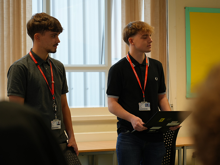 Two males stood presenting to an audience, one of them holding a laptop