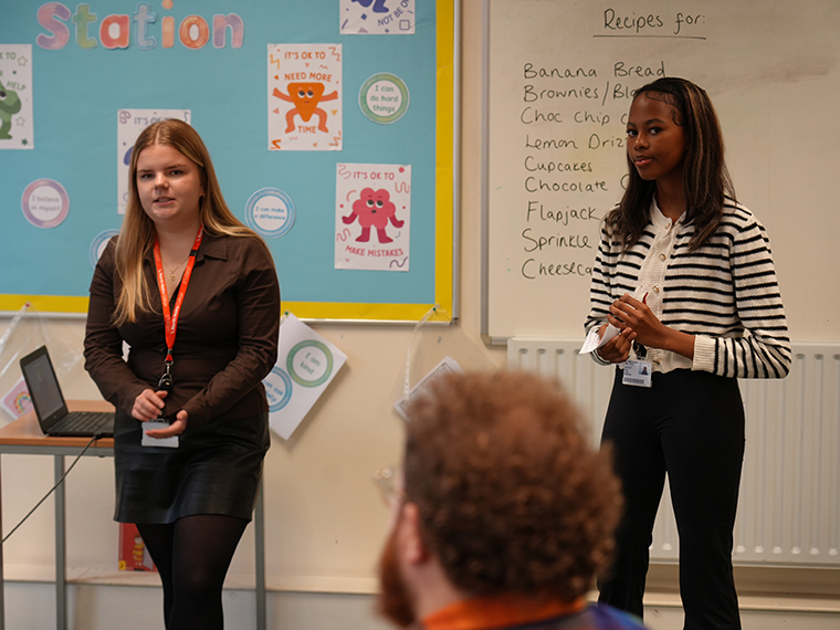 Two females stood presenting to an audience, a whiteboard behind them
